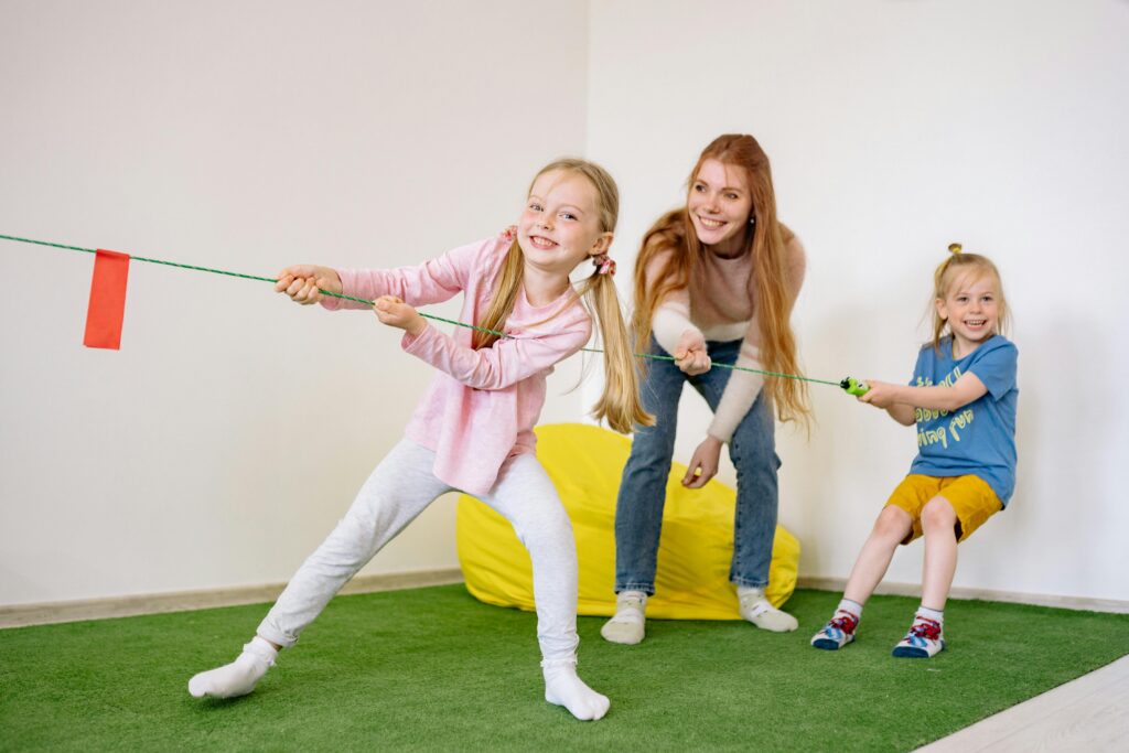 pexels photo 8613179 8613179 Kids and teacher enjoying a fun tug-of-war game in an indoor playroom setting.